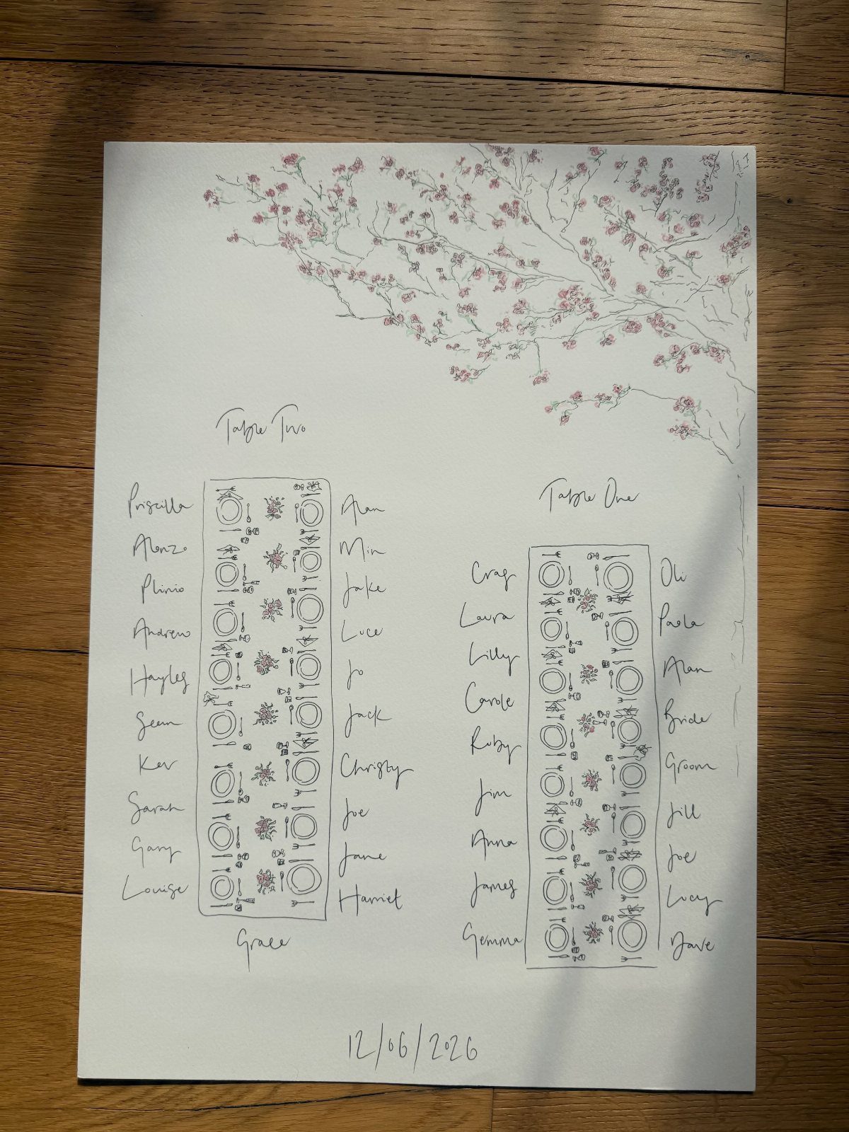 Hand-drawn wedding seating chart with two rectangular tables and guest names on paper.