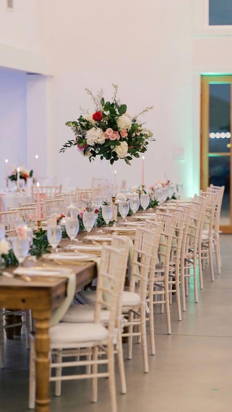 Long wooden wedding table with white chairs and elegant floral centerpieces