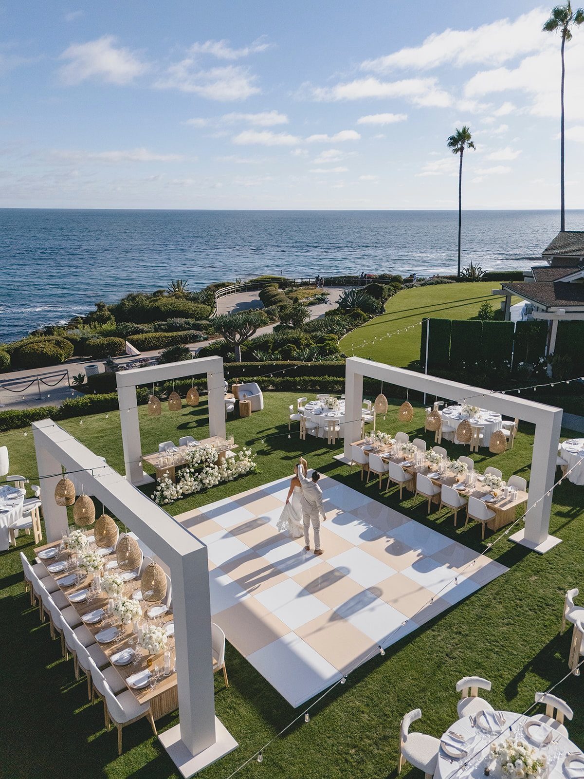 Wedding reception tables and dance floor on a lawn overlooking the blue ocean