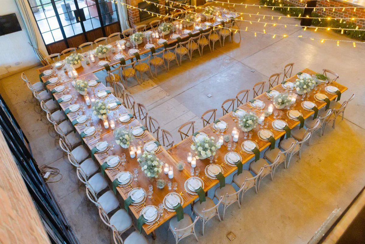 U-shaped arrangement of long wooden wedding tables with white floral centerpieces and chairs