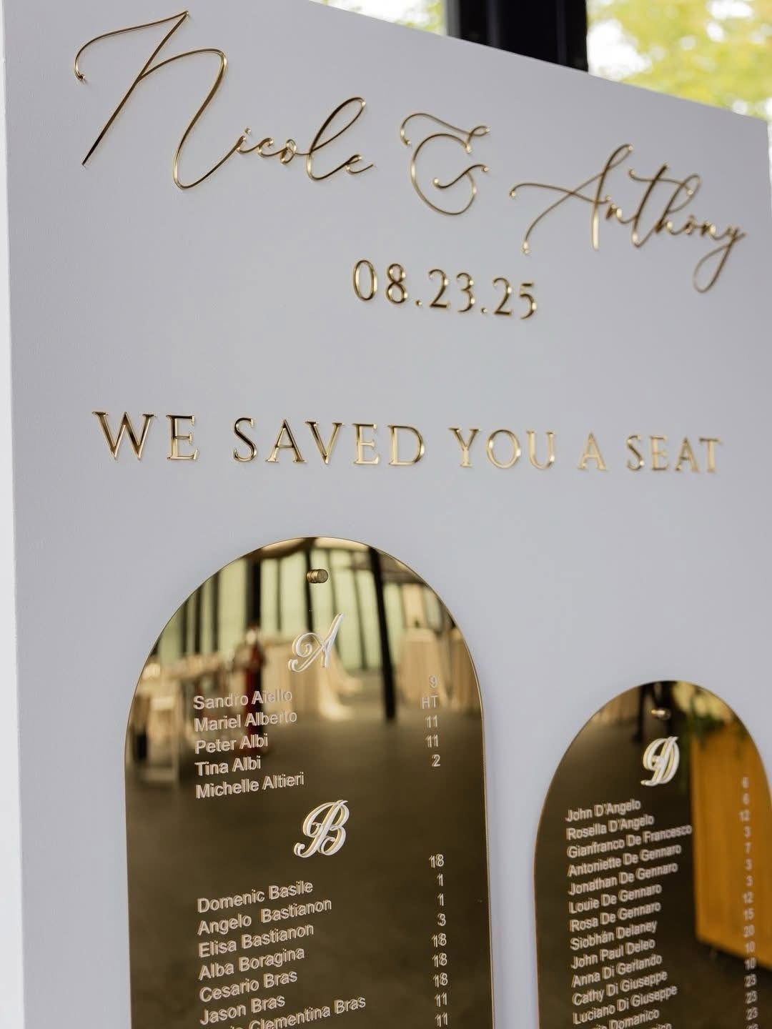 White wedding seating board with gold mirrored acrylic arches listing guest names.