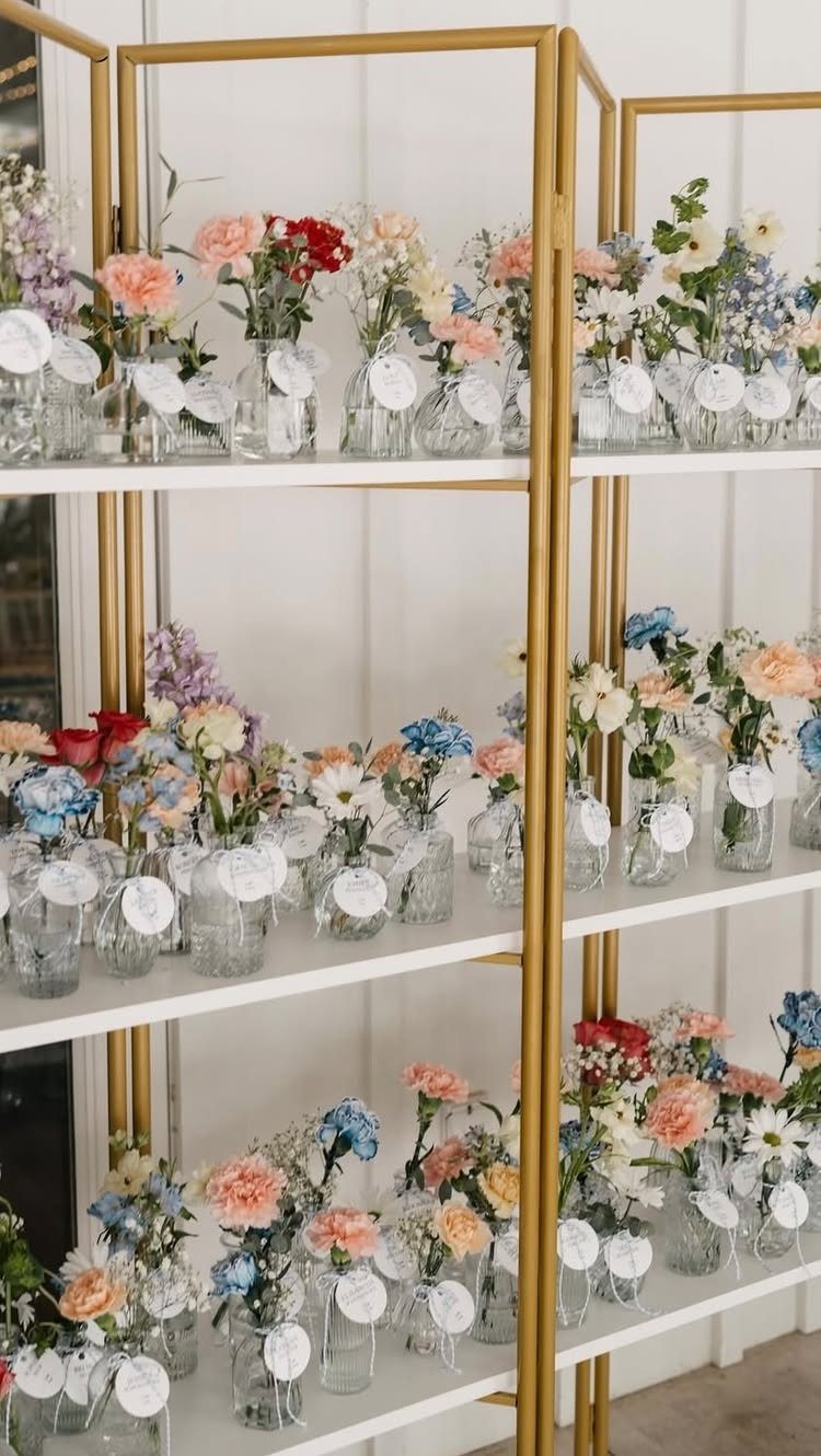 Gold shelving unit with small flower vases and white circular escort cards for wedding seating.