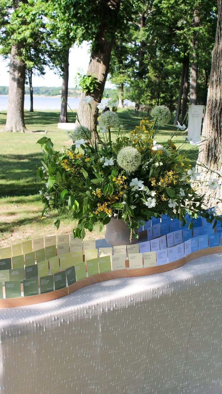 Floral arrangement and colorful escort cards on a white table in a wooded area