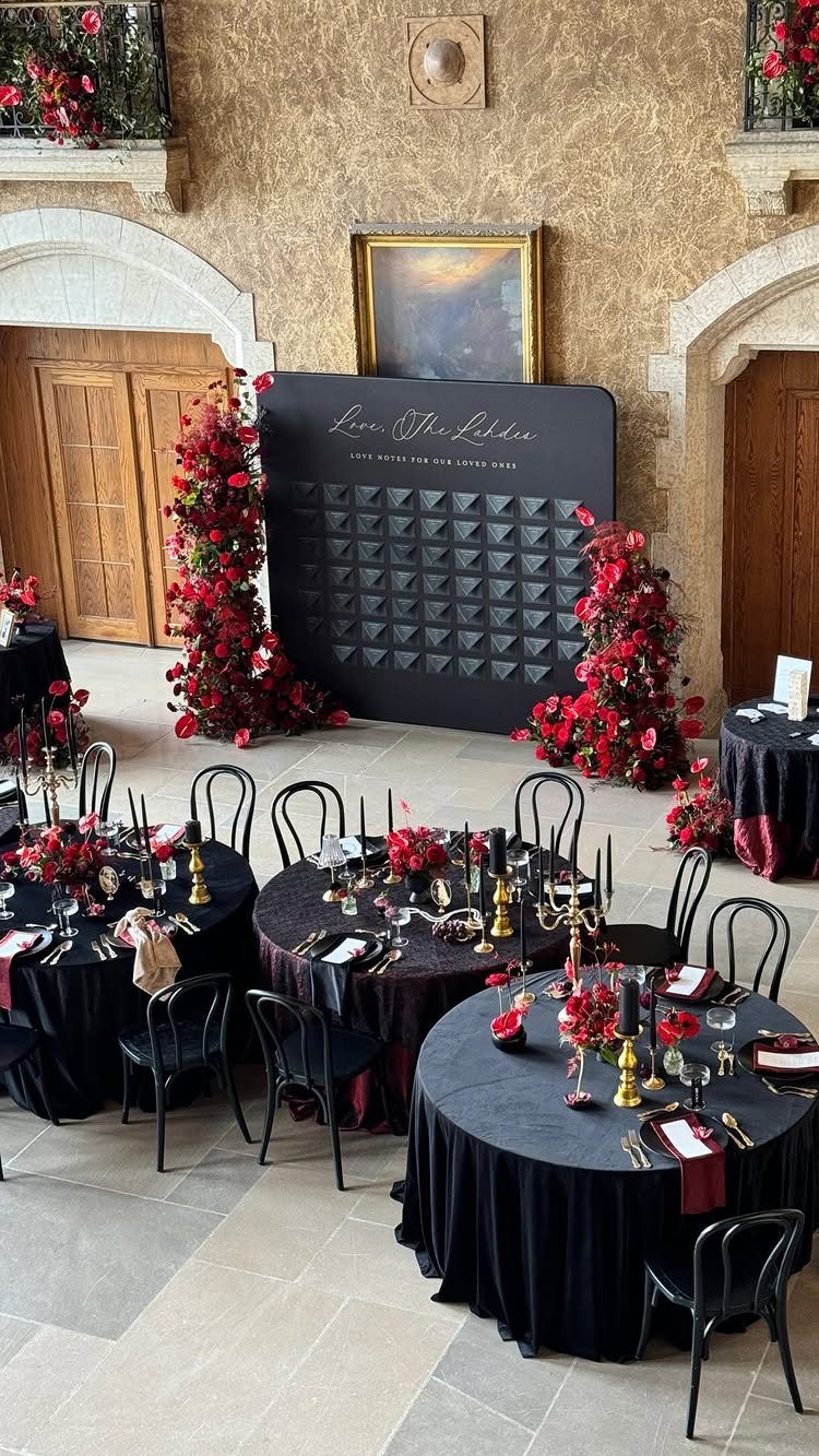 Black escort card display wall with red flowers and black wedding table settings.