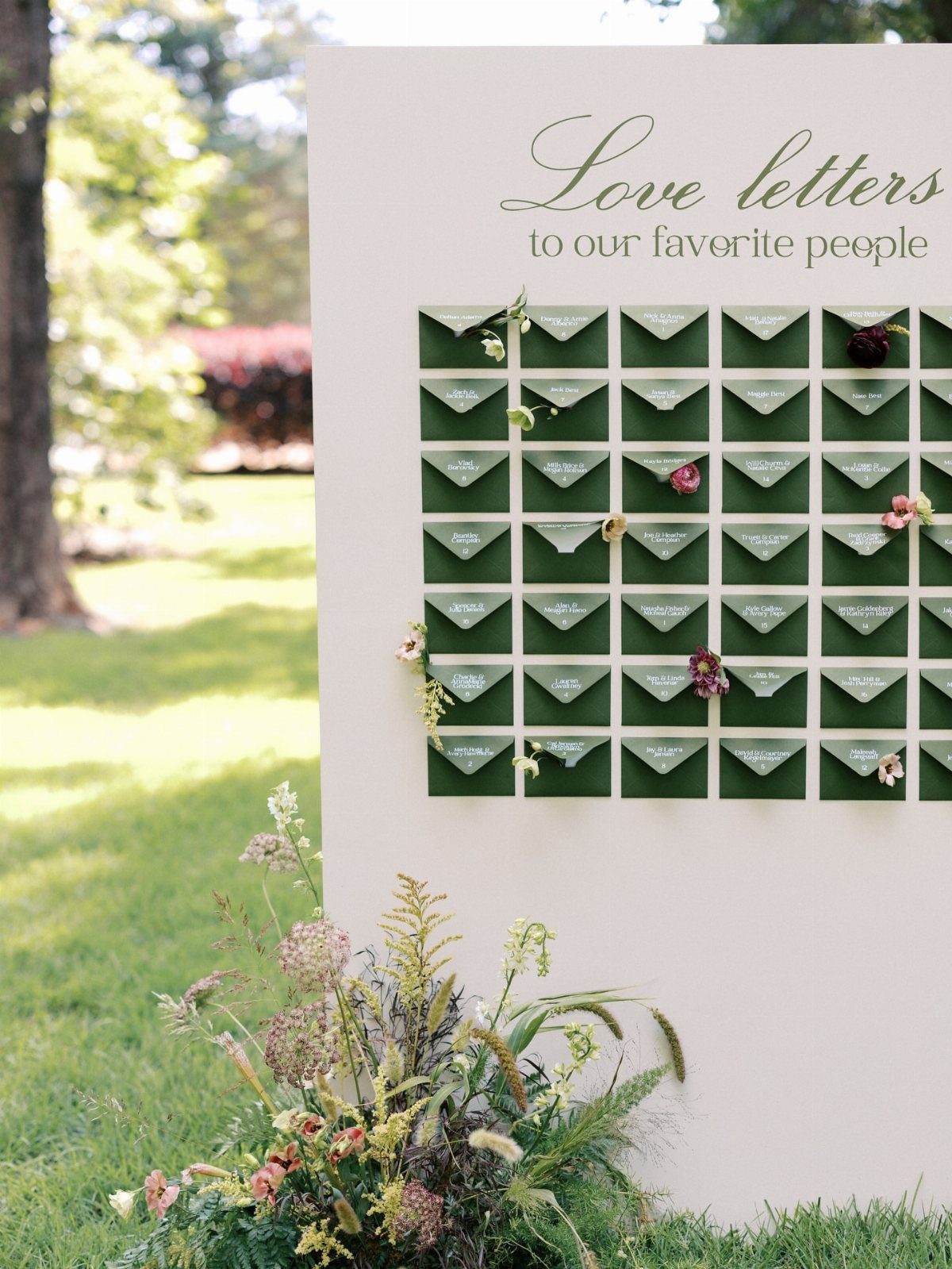 White display board with green envelopes and floral arrangement on a grassy lawn.