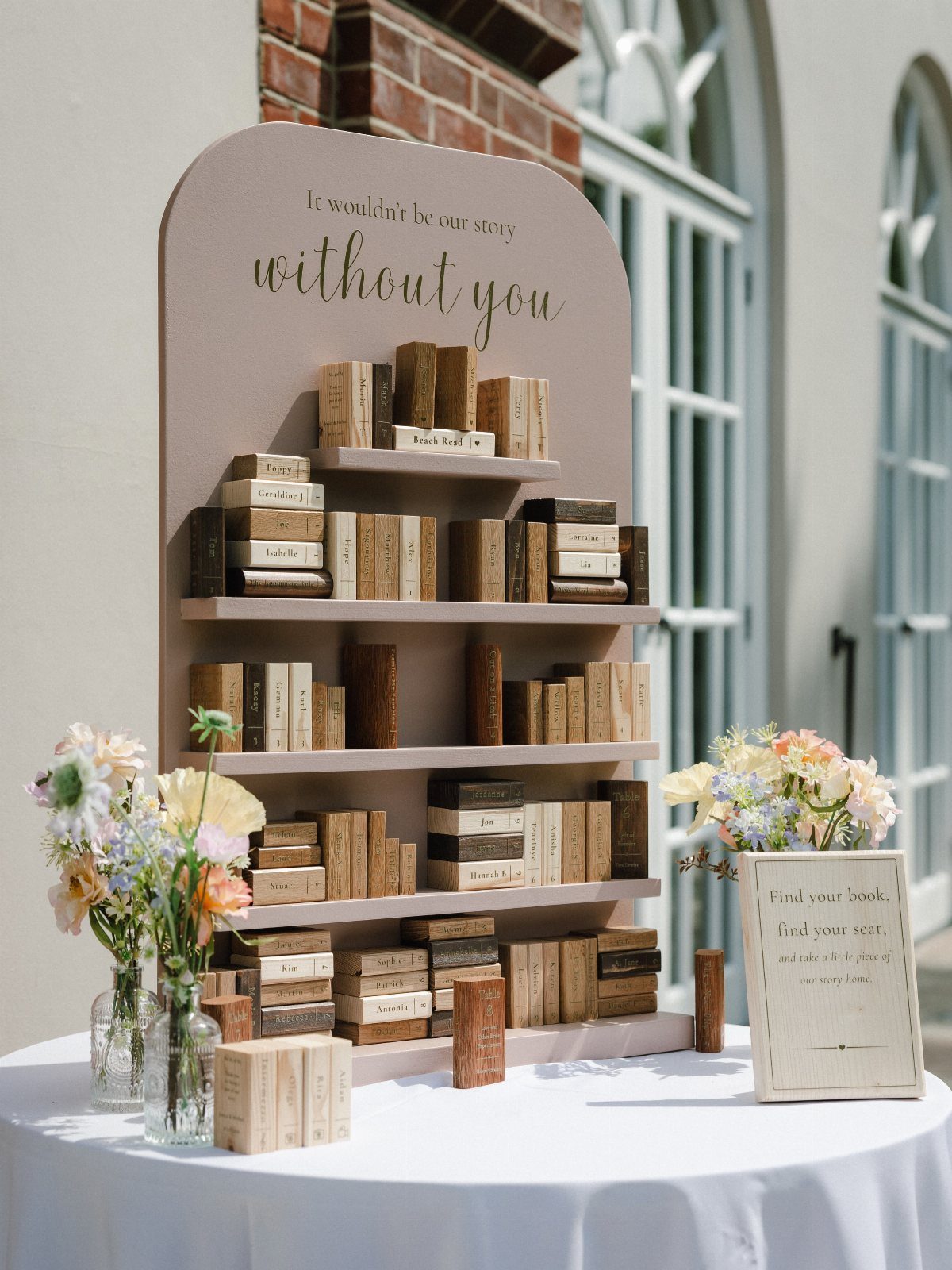 Arched beige seating chart with wooden book-shaped blocks on shelves and floral accents.