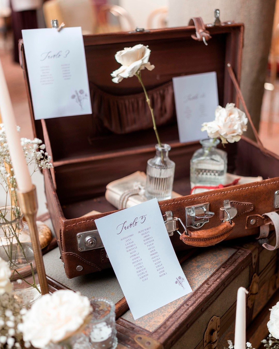 Open brown vintage suitcase holding wedding seating cards and white roses.