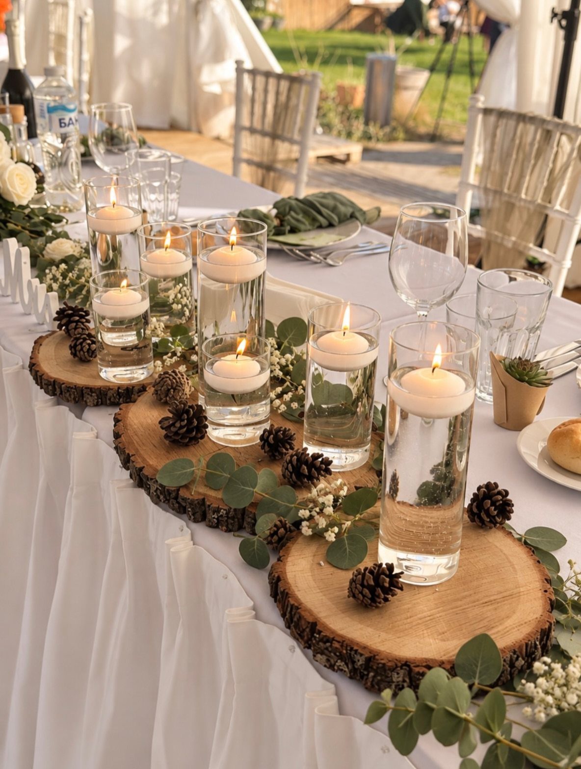 Floating white candles in glass cylinders on wooden slices with eucalyptus greenery garlands