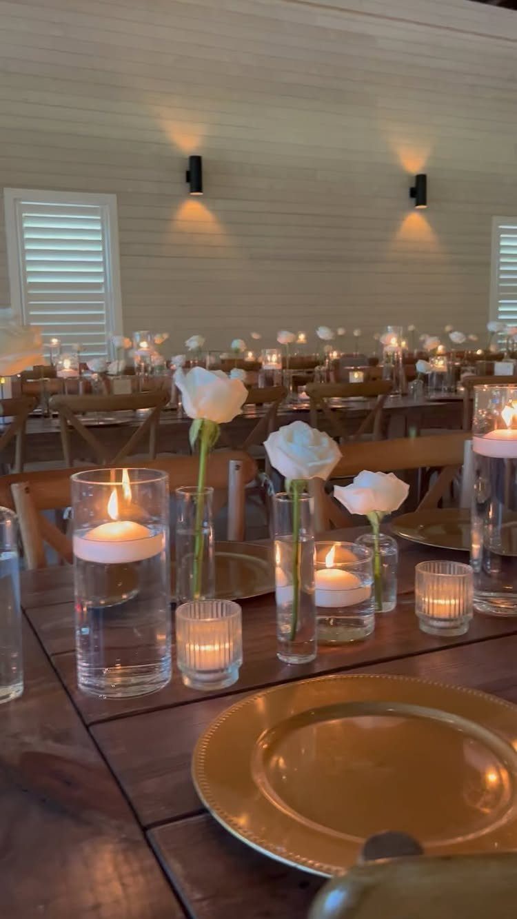 Floating candles and single white roses in glass vases on a wooden wedding table