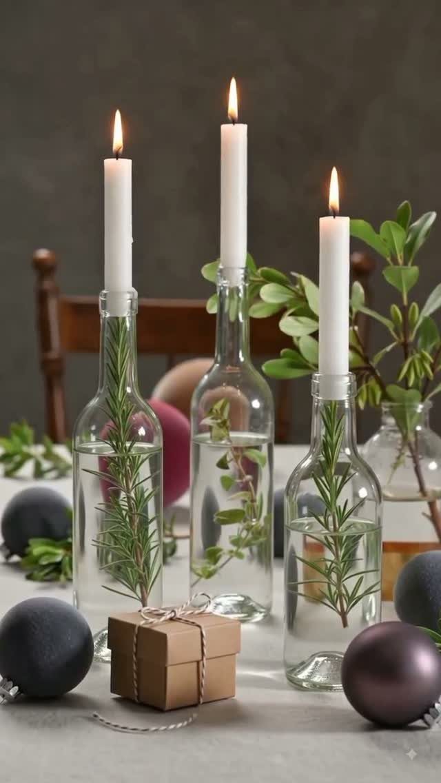Clear glass wine bottles holding lit white taper candles and green rosemary sprigs.