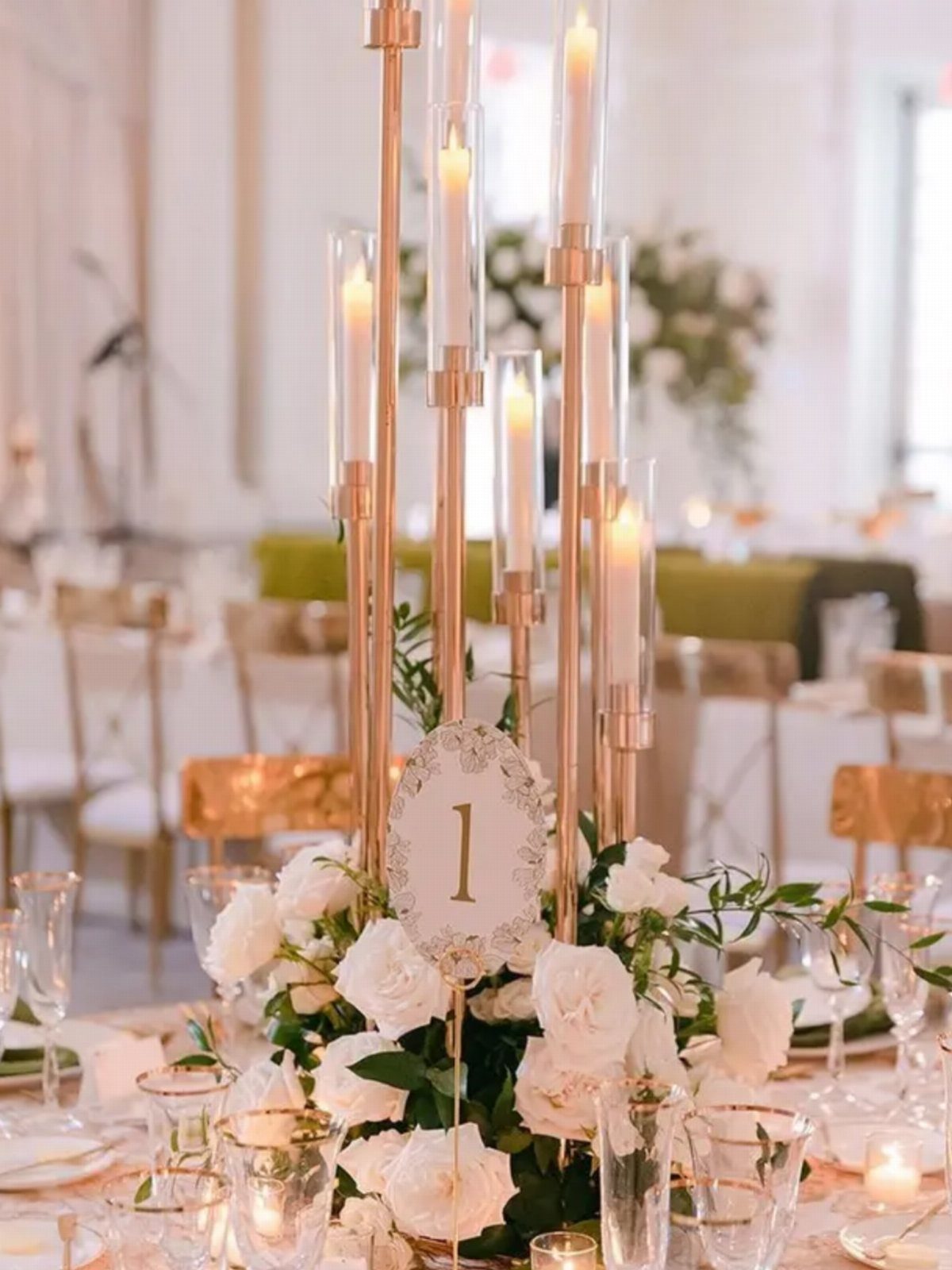 Tall gold candle holders with white roses and greenery on a wedding table.