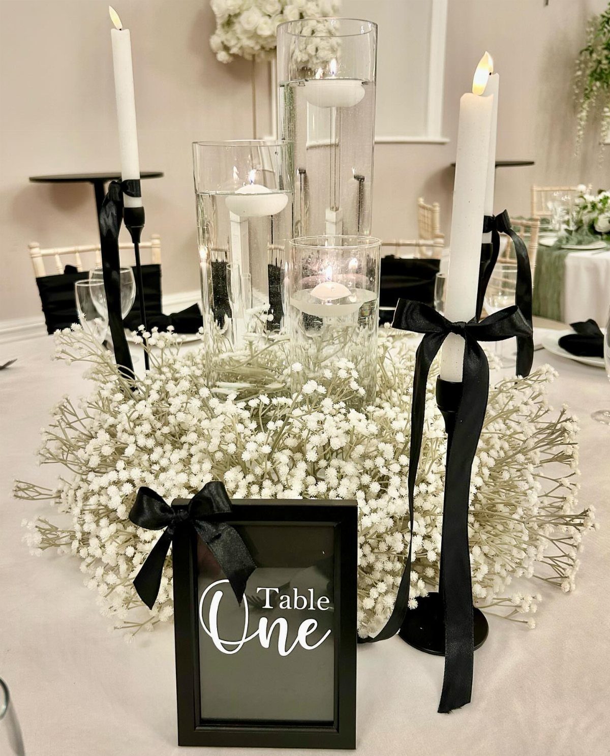 White baby's breath and candles with black ribbons on a wedding table.