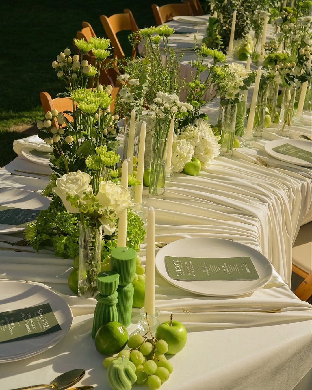 Green apples and grapes mixed with white roses and candles on a wedding table.