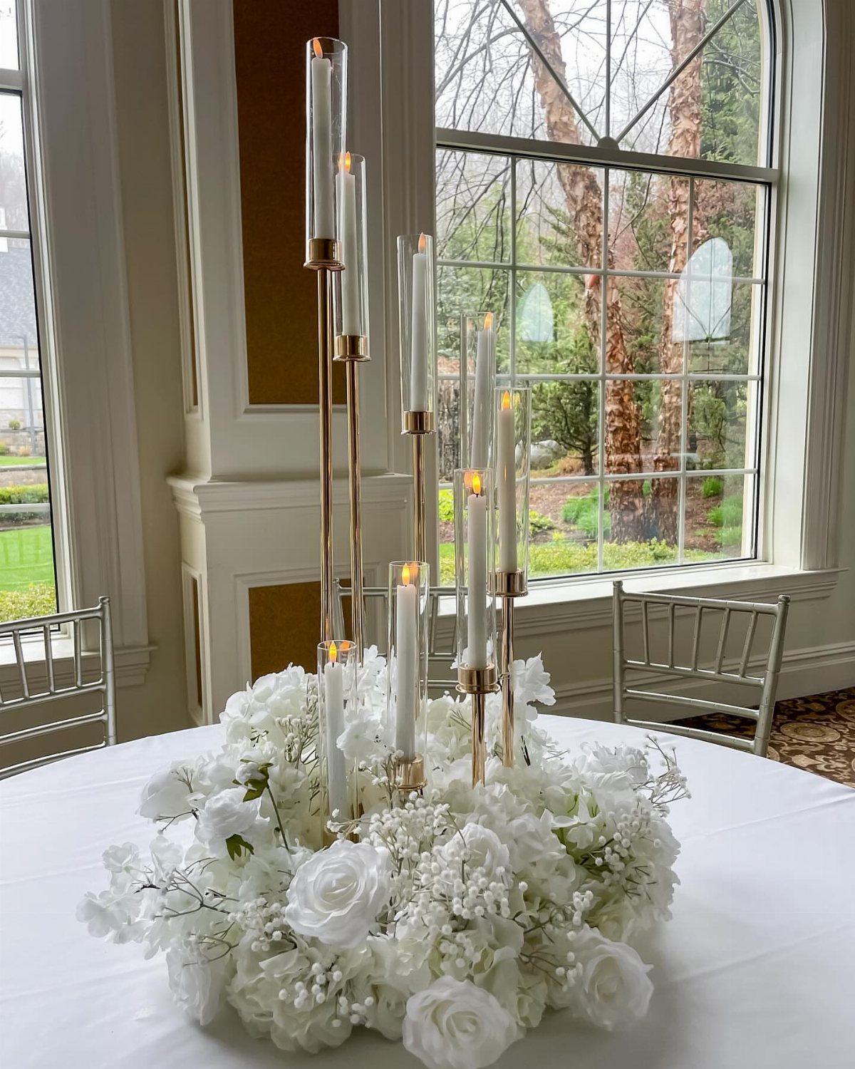 Gold slender candle holders with white candles surrounded by white roses and baby's breath.