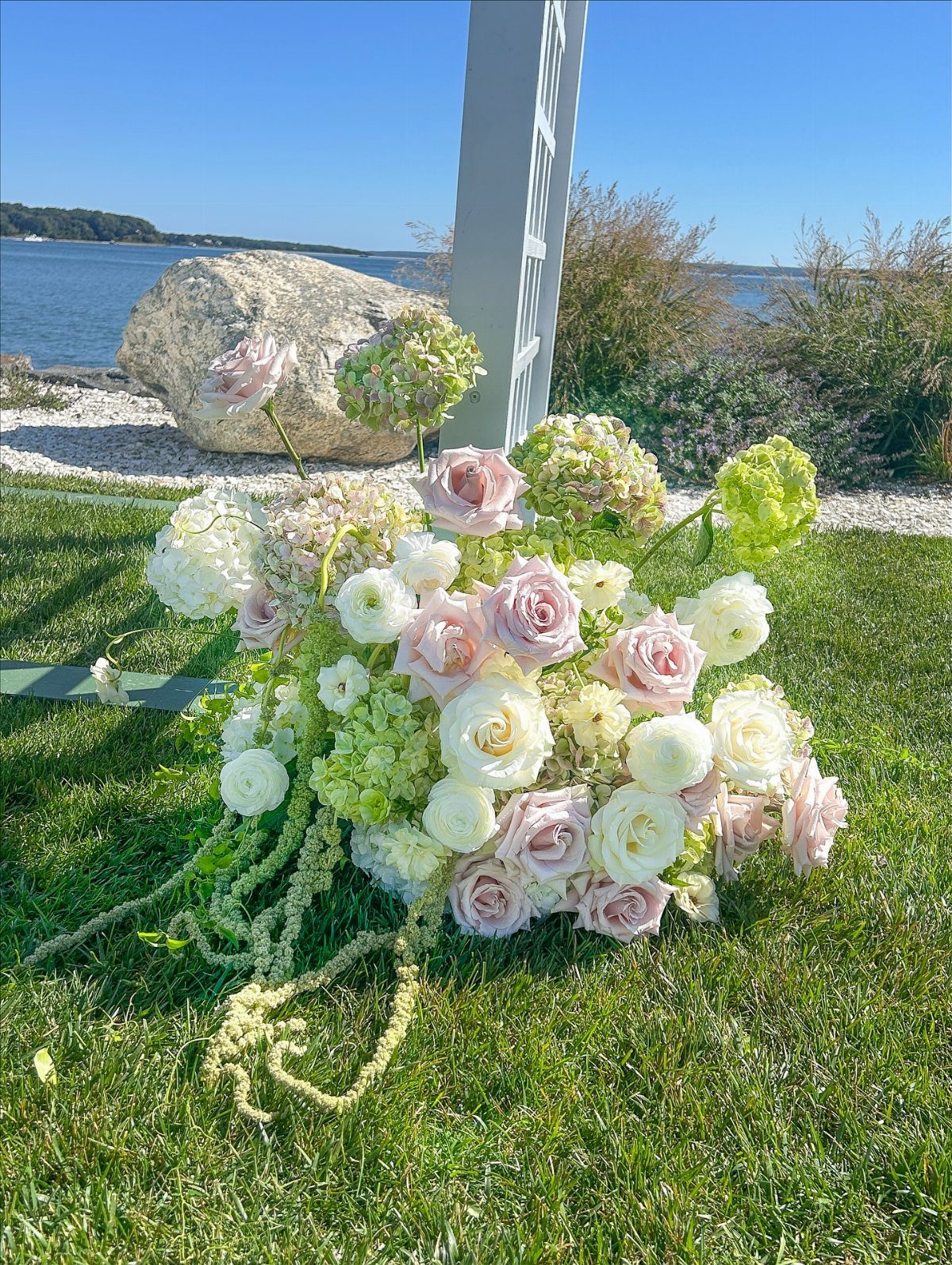 Wedding bouquet with pink and white roses on grass by the ocean shore.
