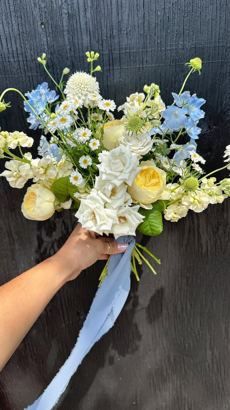 Wildflower wedding bouquet with white roses and blue flowers tied with blue ribbon.