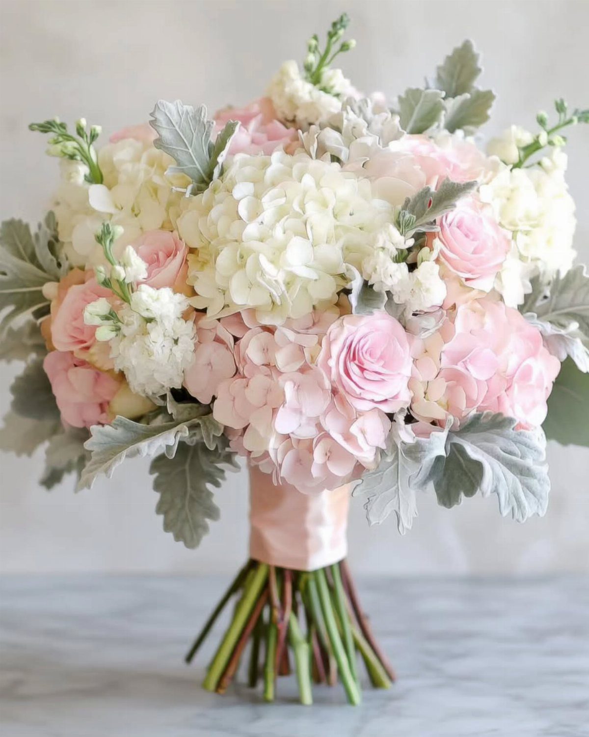 Wedding bouquet with white and pink hydrangeas, roses, and silvery dusty miller leaves.