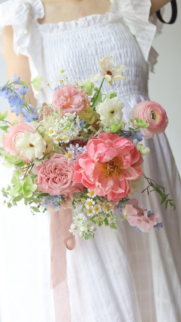 Lush wedding bouquet with pink peonies and blue flowers held by a bride.