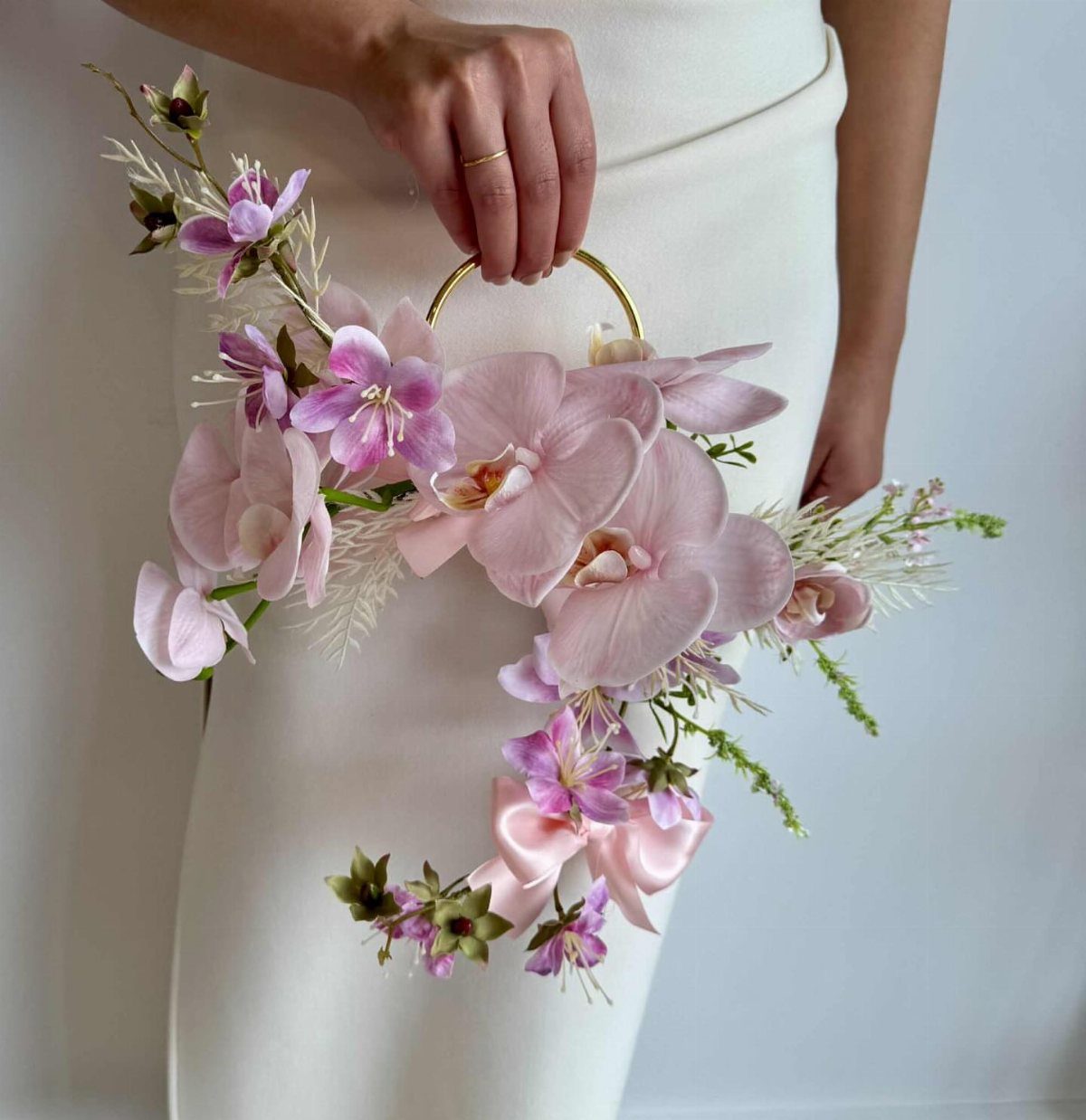 Pink and purple orchid wedding bouquet with a gold circular handle and ribbon.