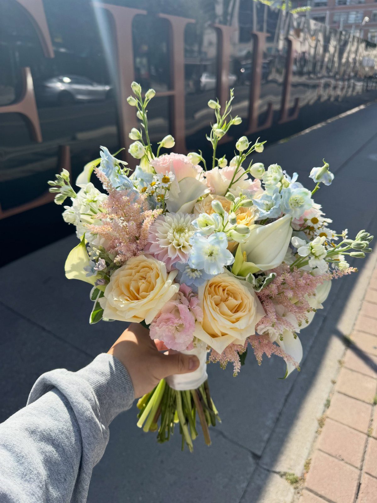 Wedding bouquet with pale yellow roses, light blue flowers, and white calla lilies.