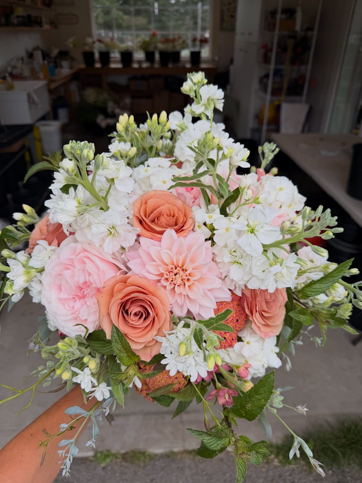 Peach and pink rose wedding bouquet with white flowers and green foliage.