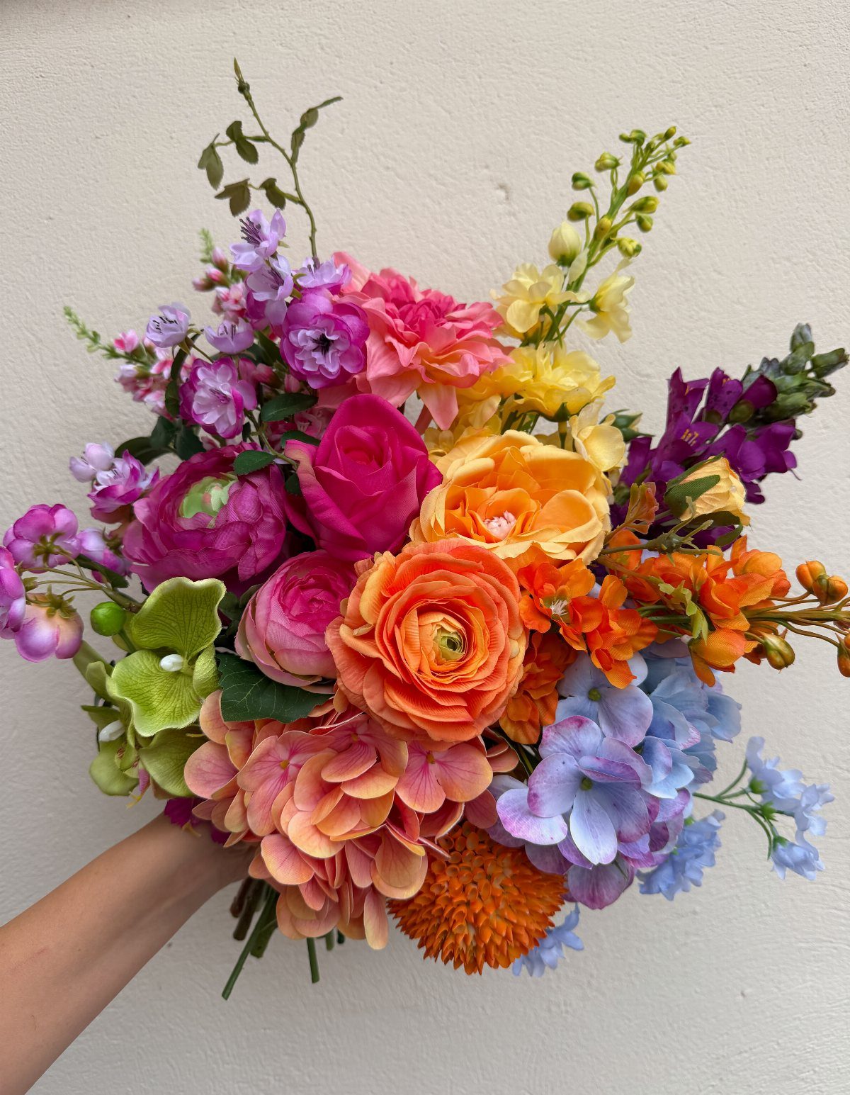 Colorful wedding bouquet with pink, orange, yellow, and blue summer blooms held by hand.