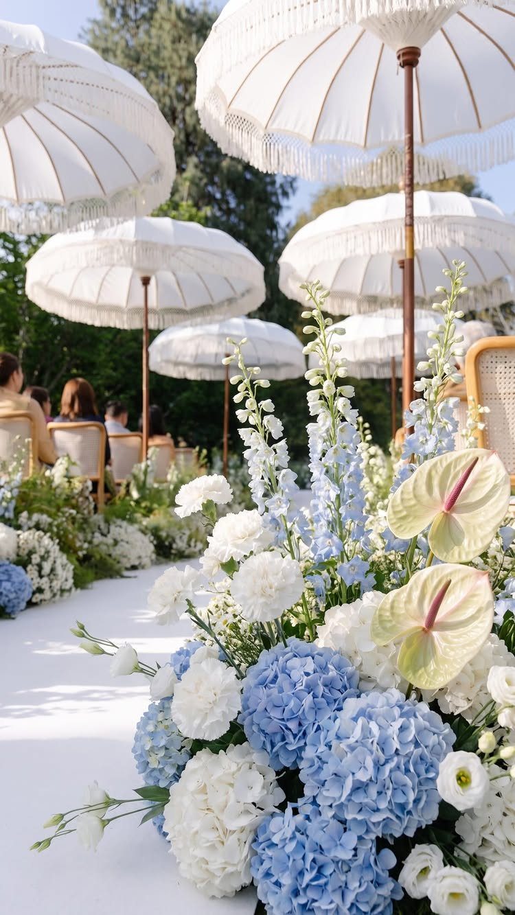 Blue and white floral arrangements lining a wedding aisle with white parasols.
