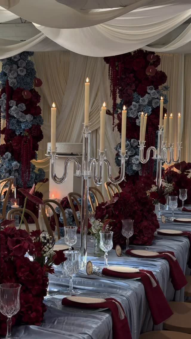Wedding table with dusty blue linens, burgundy napkins, and deep red floral arrangements.