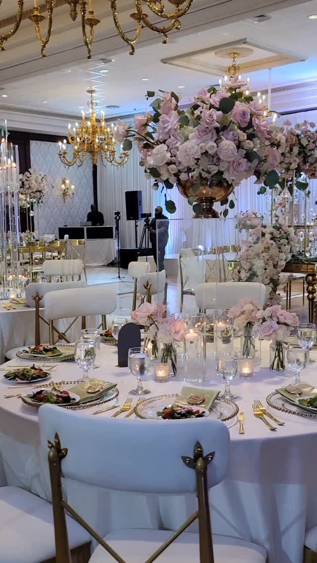 Wedding reception table with pink floral centerpieces, gold accents, and white chairs.