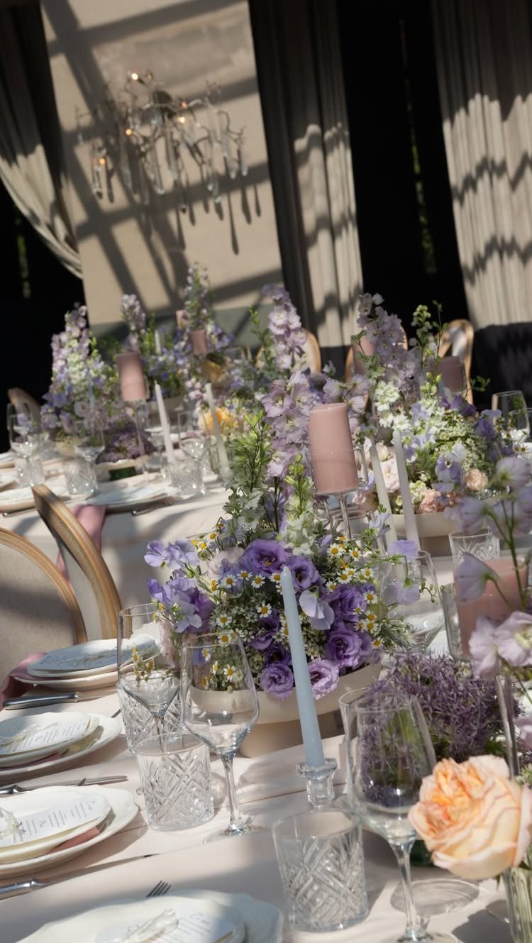 Wedding table setting with ivory linens and lavender floral centerpieces and purple candles.