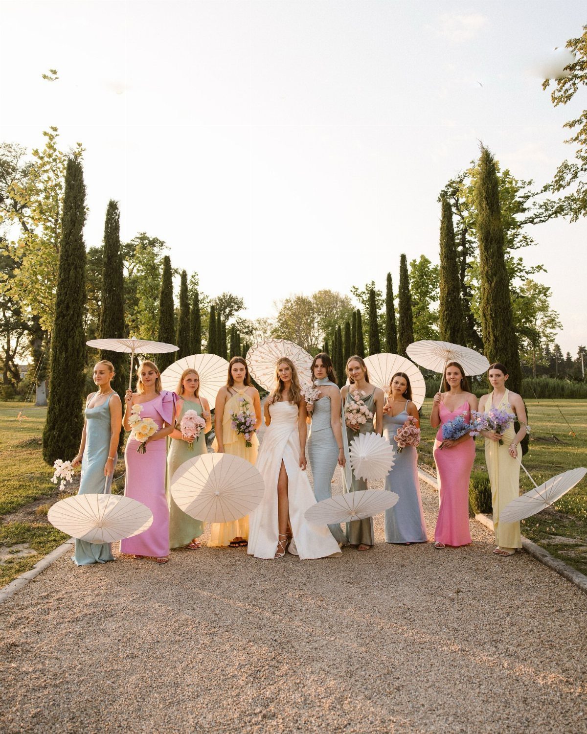 Bride and bridesmaids in colorful pastel dresses posing with white parasols in a garden