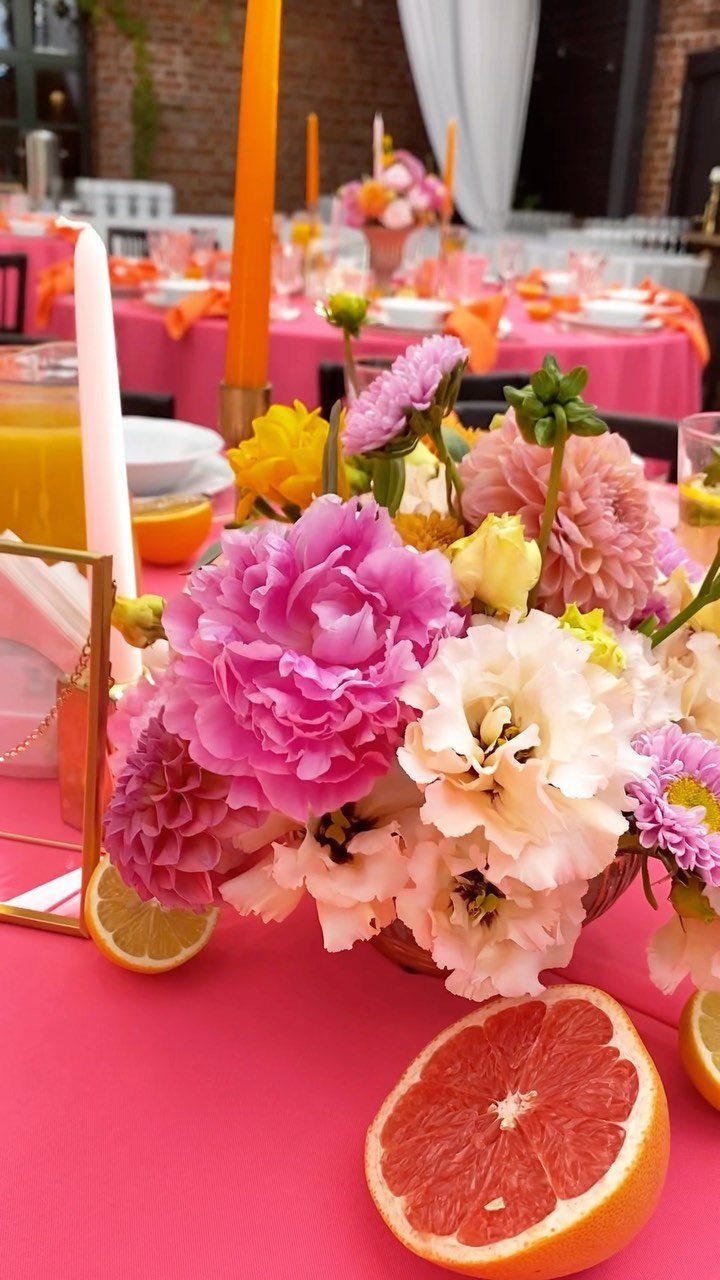 Pink and orange wedding table setting with floral centerpiece and citrus fruit slices.