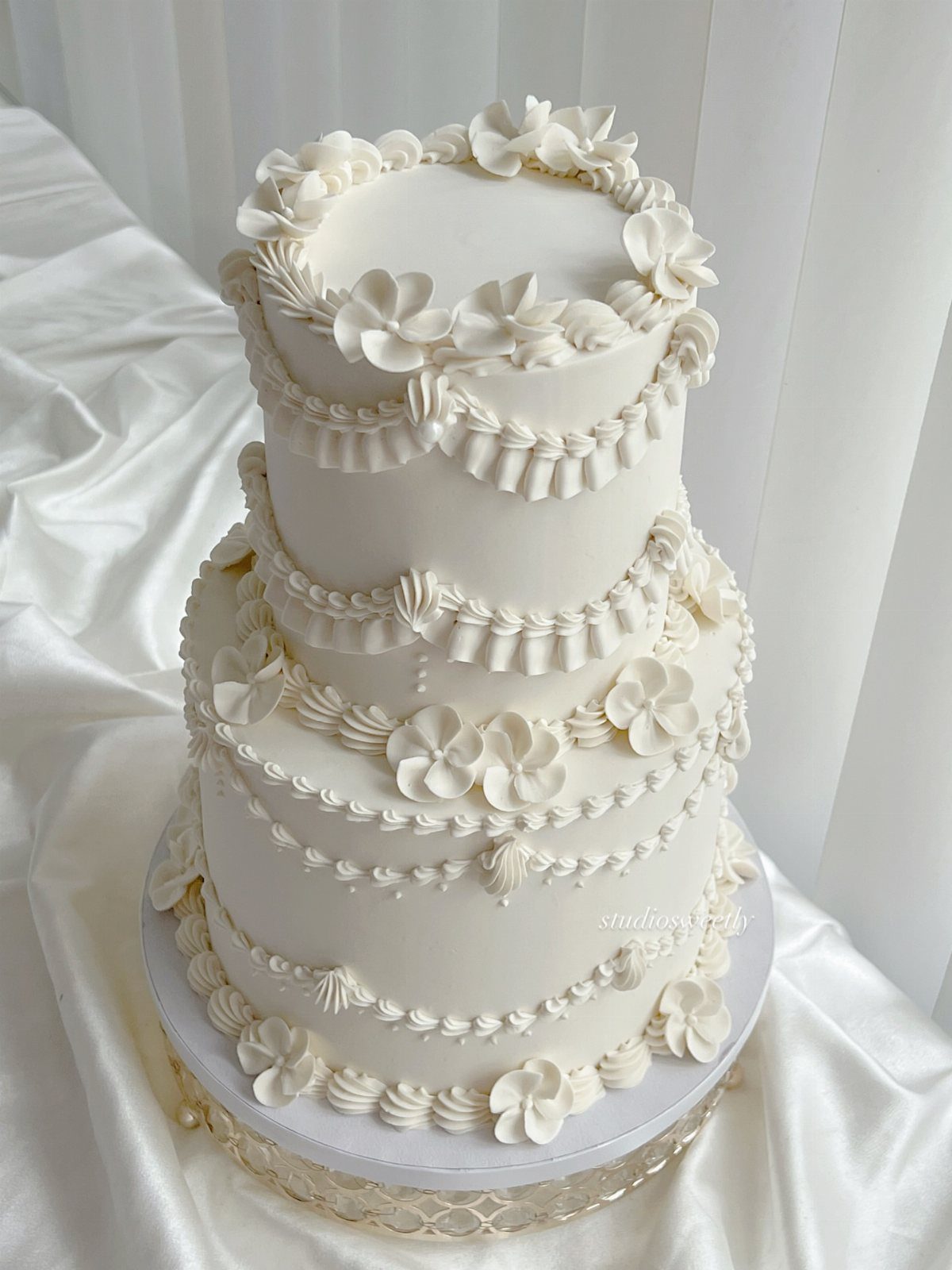 Ivory wedding cake with floral frosting on a white satin draped background