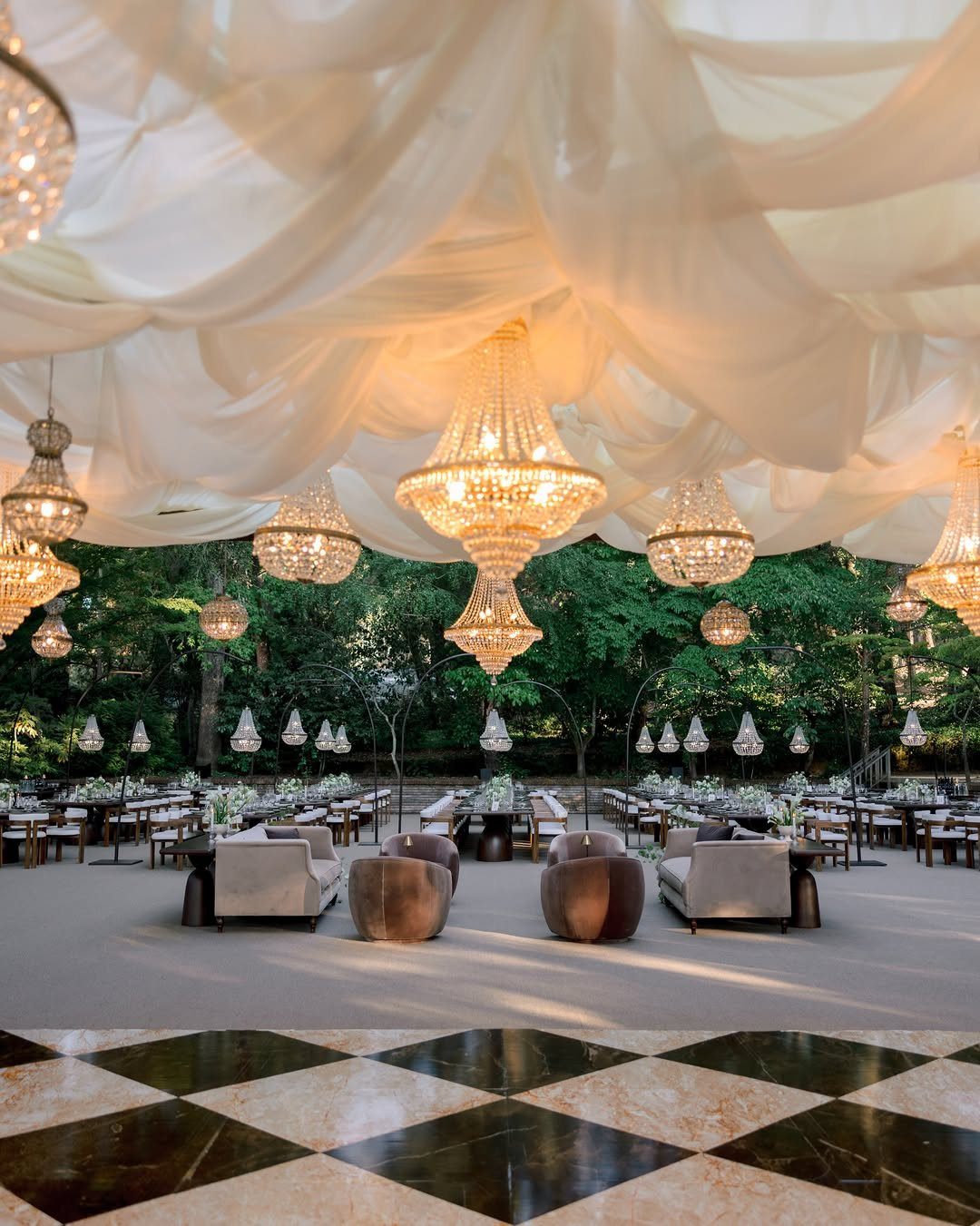 Ornate crystal chandeliers hanging from a draped white fabric ceiling over a dance floor.