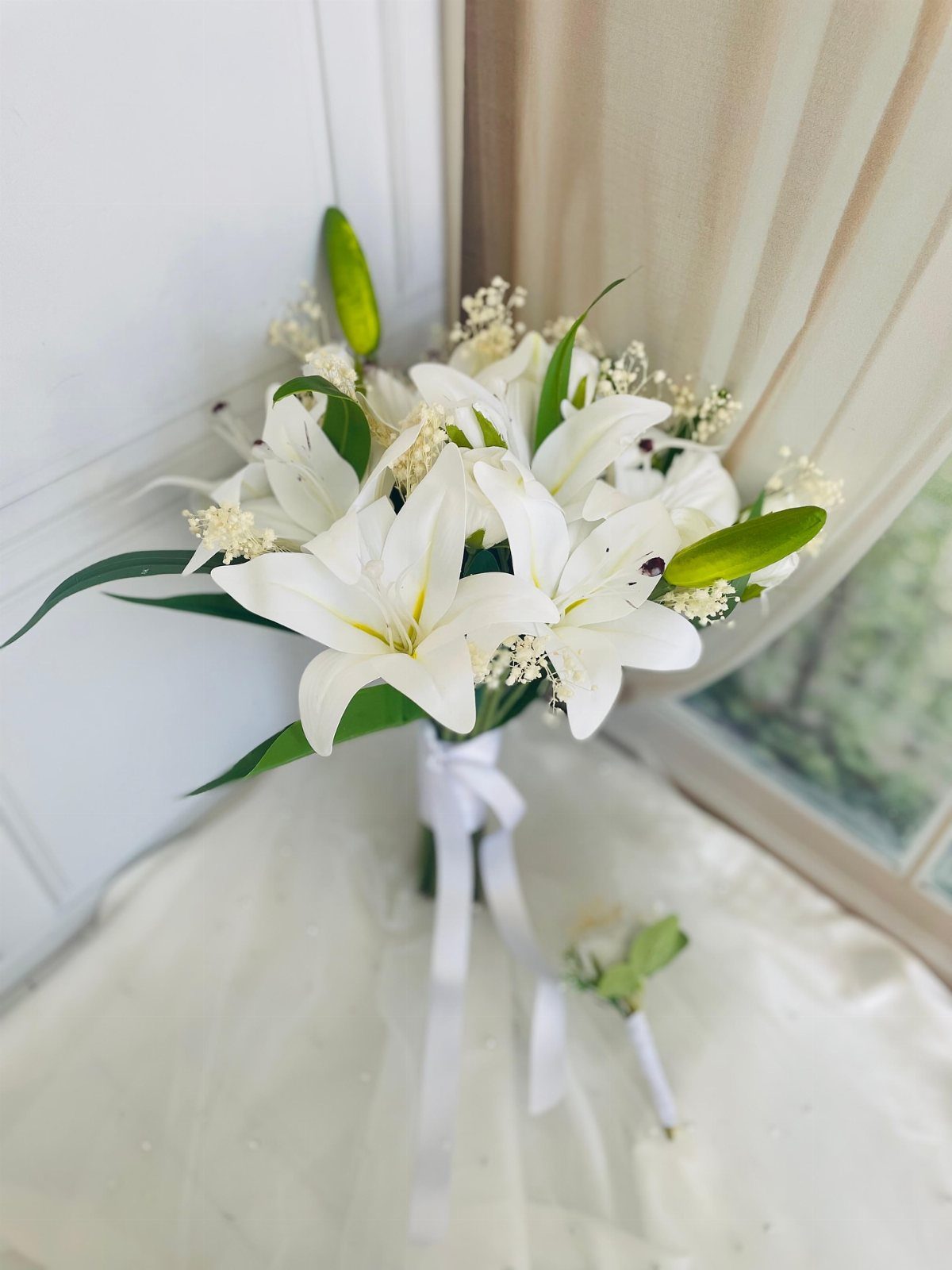 White lily bridal bouquet tied with a white ribbon on white fabric.
