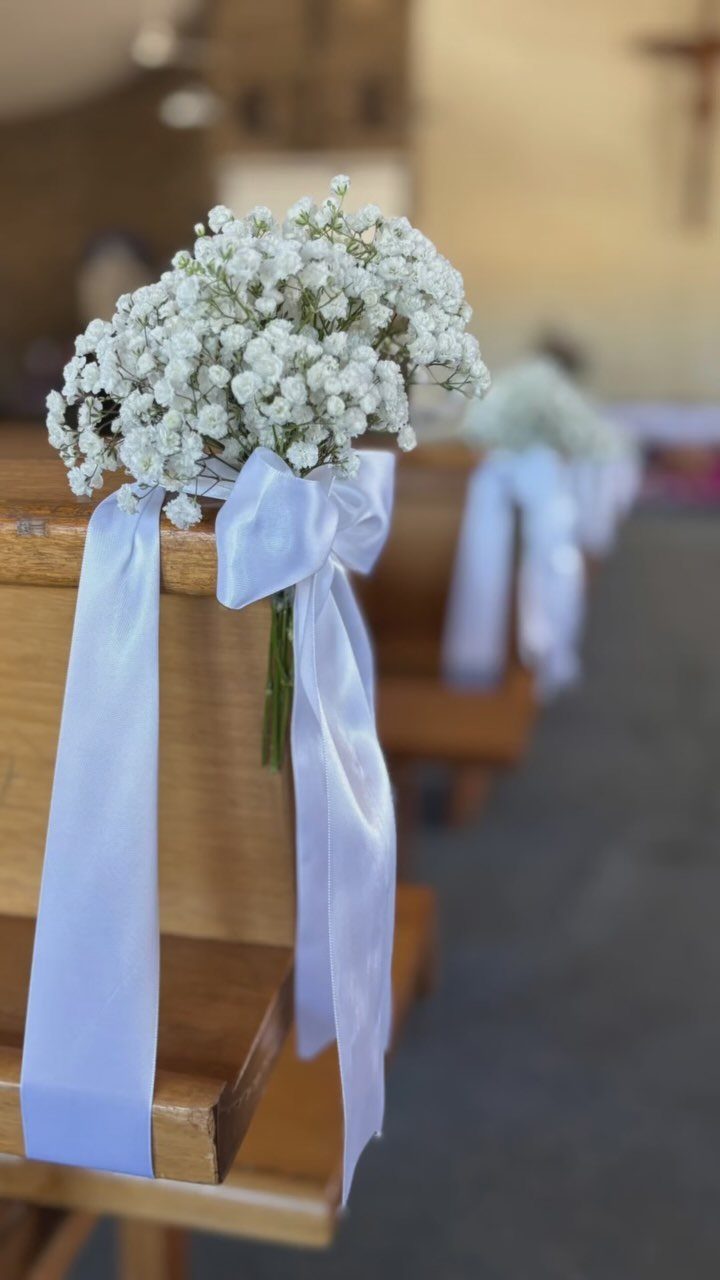 White baby's breath bouquets with satin ribbons decorating wooden church pews.