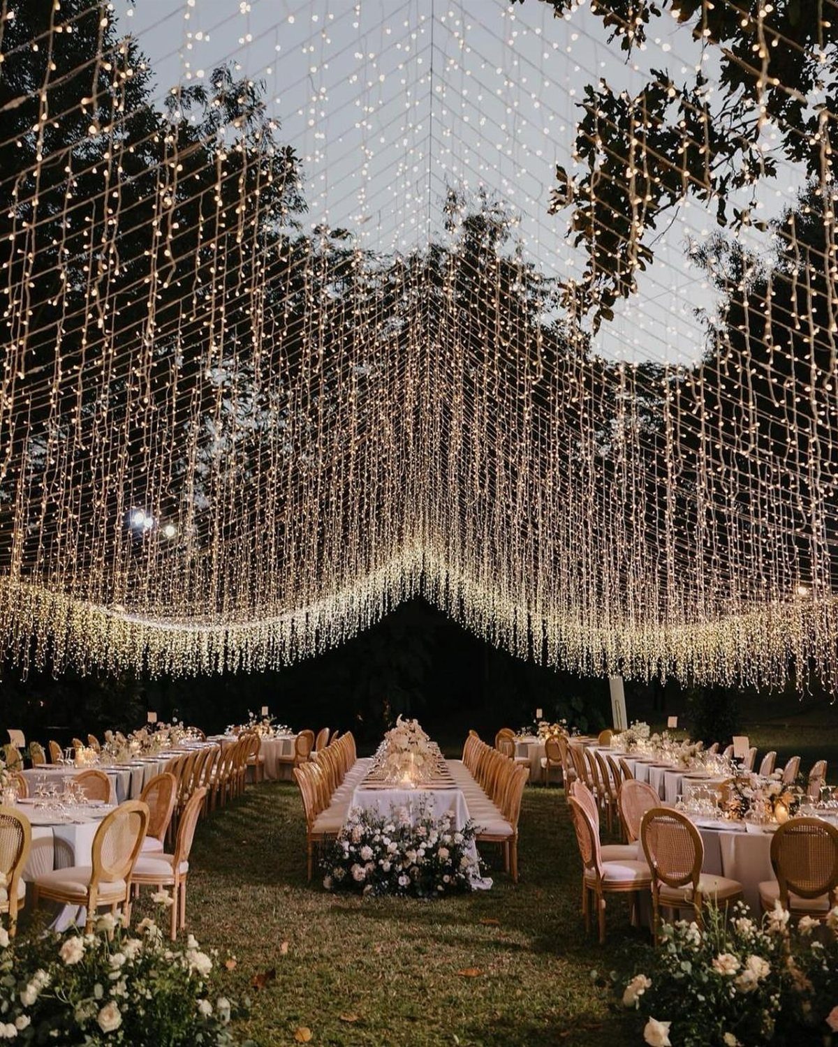 Outdoor wedding reception with a dense canopy of warm white string lights overhead.