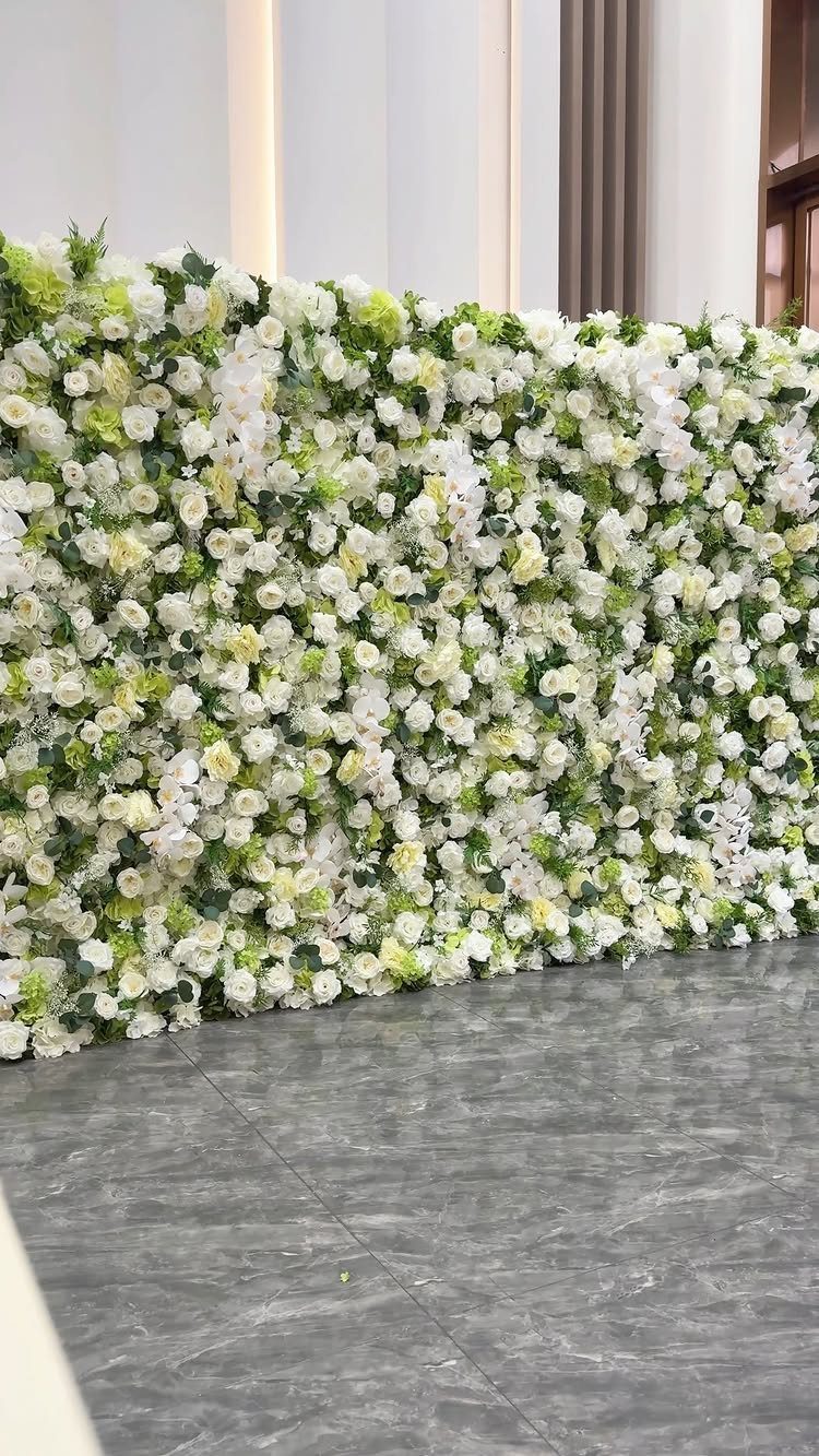 Floral backdrop wall made of white and cream flowers with green leaves.