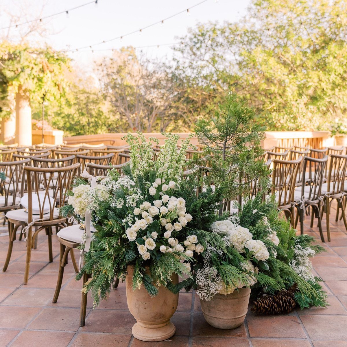 Potted white flowers and greenery arrangements on a terracotta floor at an outdoor wedding.