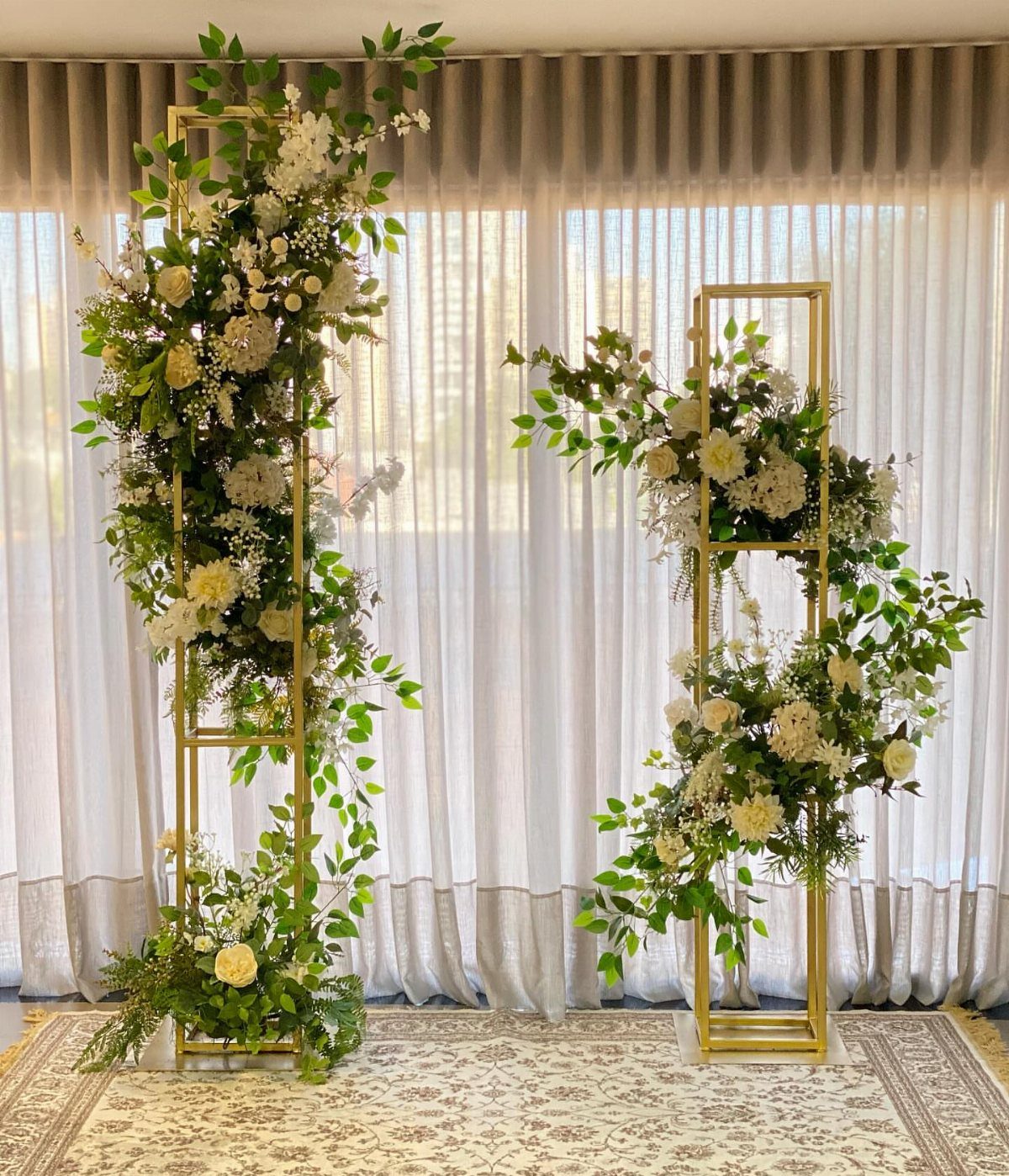 Gold metal frames adorned with white flowers and greenery for a wedding altar.