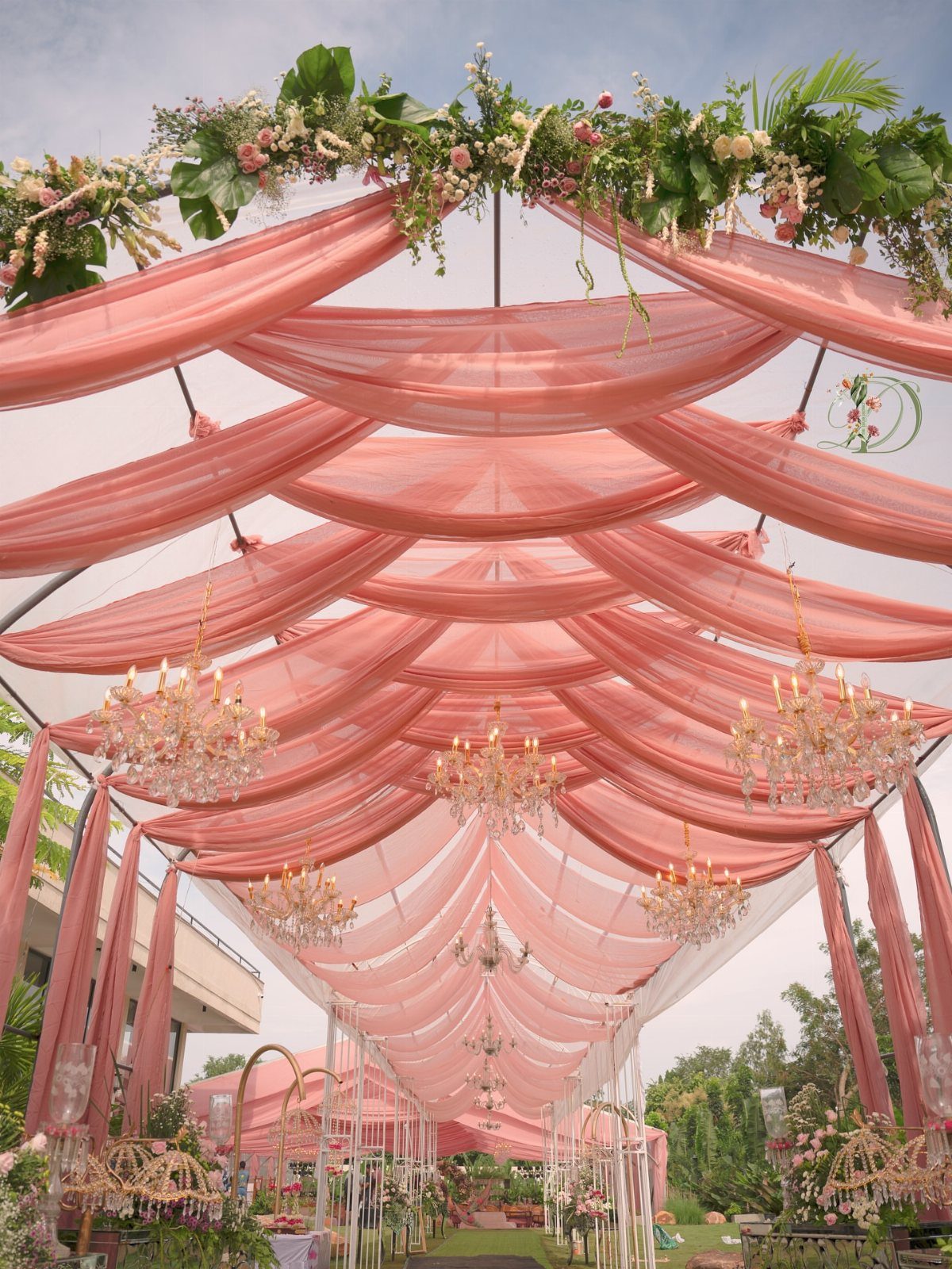 Peach tulle fabric draped across a ceiling with crystal chandeliers and floral accents.