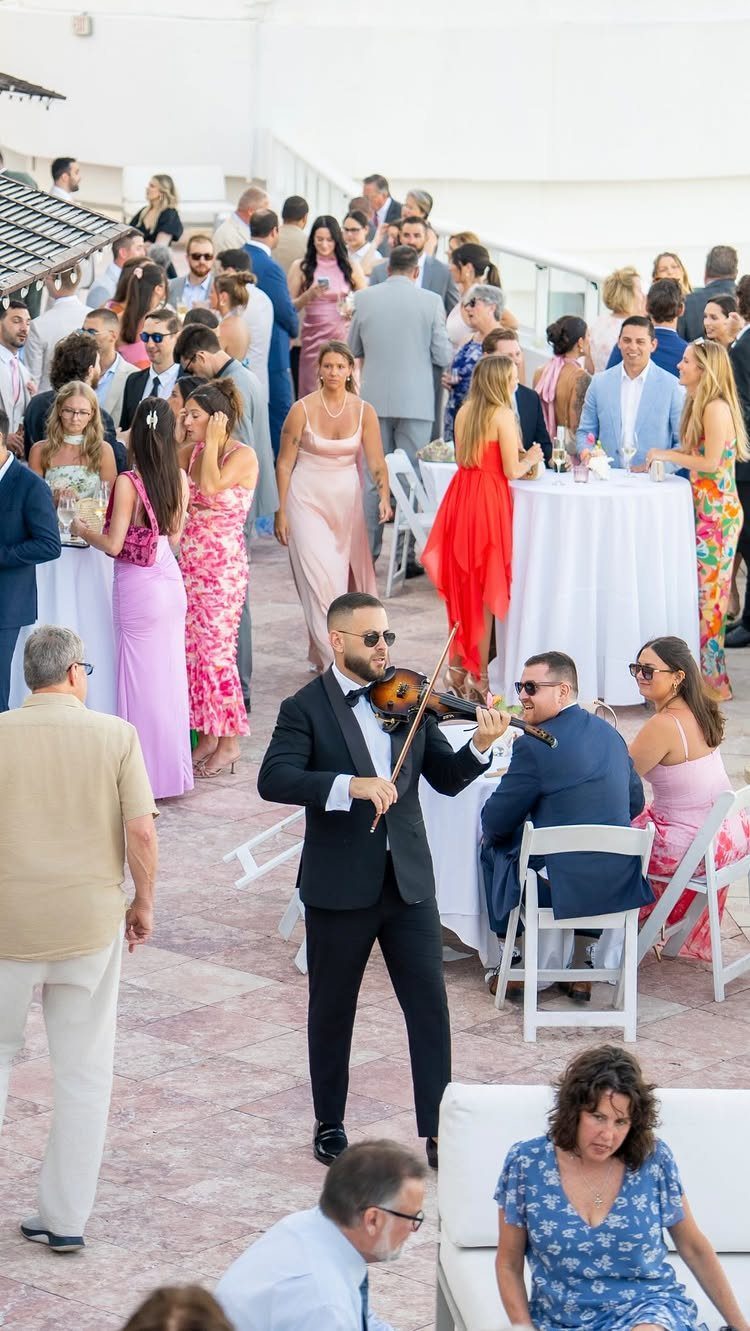 Violinist in a tuxedo playing for guests at an outdoor wedding cocktail reception.