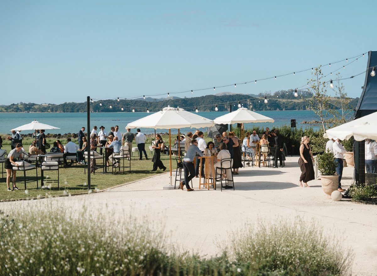 Outdoor wedding reception featuring high-top and lower tables under white umbrellas by the sea.