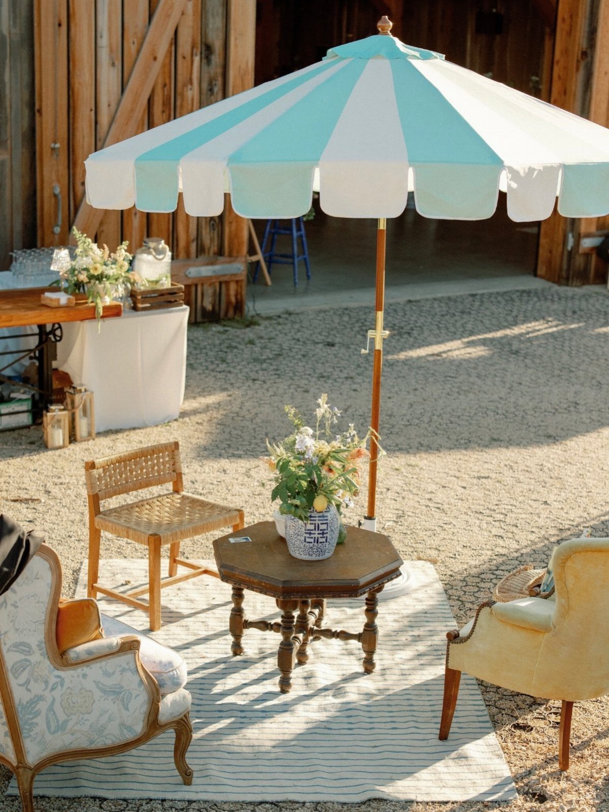 Outdoor lounge area with striped umbrella, vintage armchairs, and a small wooden table.