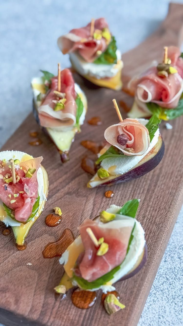 Gourmet fig and prosciutto appetizers with cheese and pistachios on a wooden board.