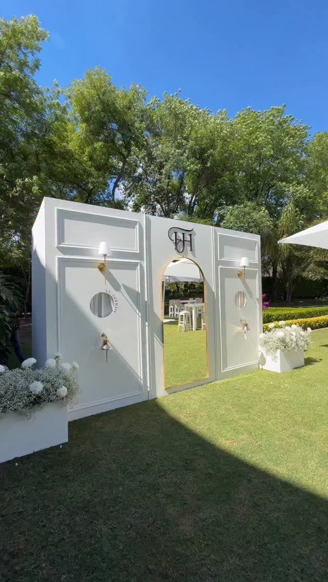 White architectural photo booth backdrop with gold mirror on a sunny green lawn
