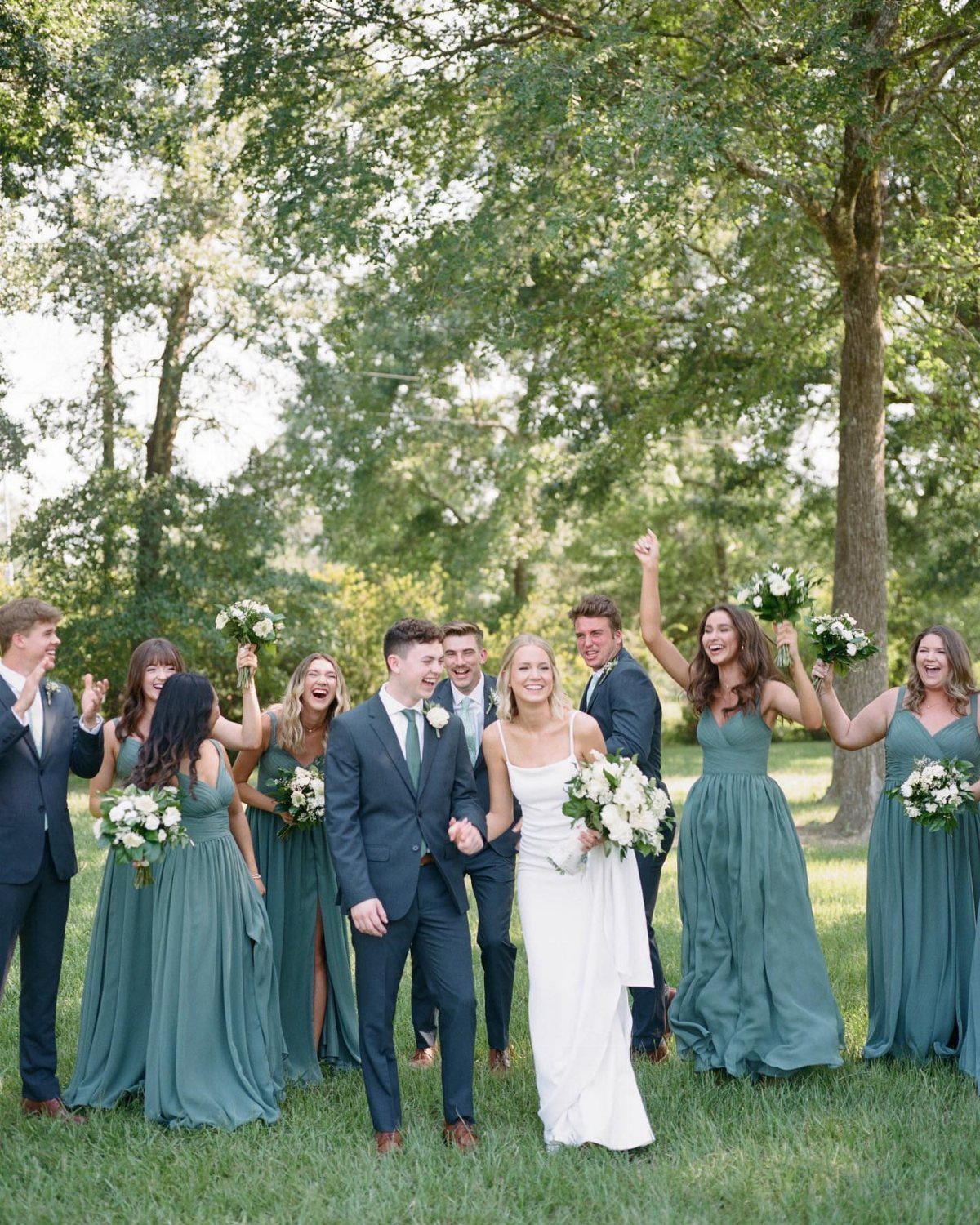 Wedding party with bridesmaids in eucalyptus green dresses and bride in white gown.