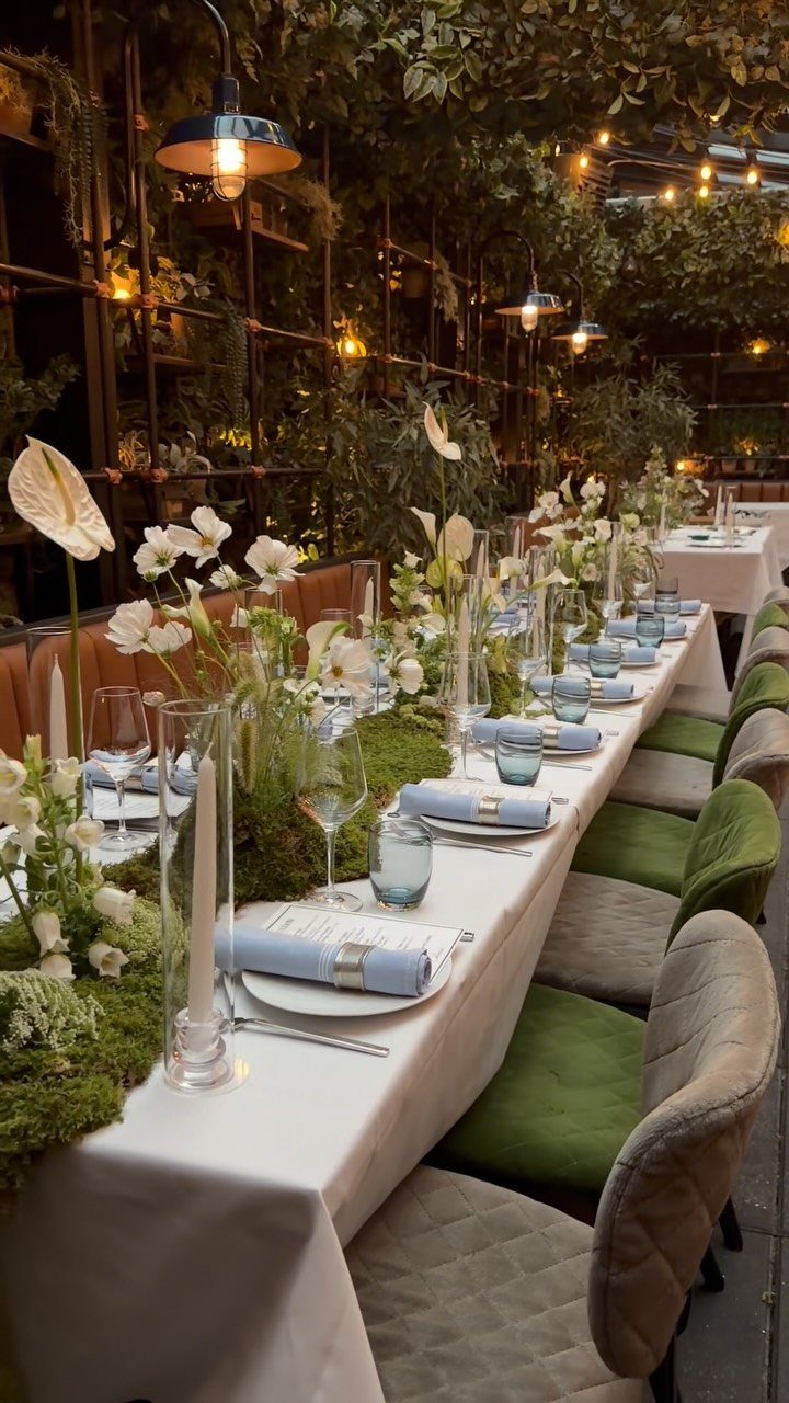 Long dining table with white linens, light blue napkins, and moss green floral centerpieces.