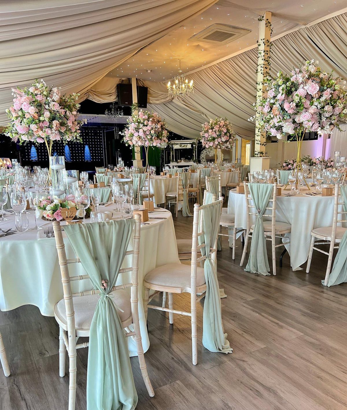 Wedding reception tables with sage green chair sashes and blush pink floral centerpieces.