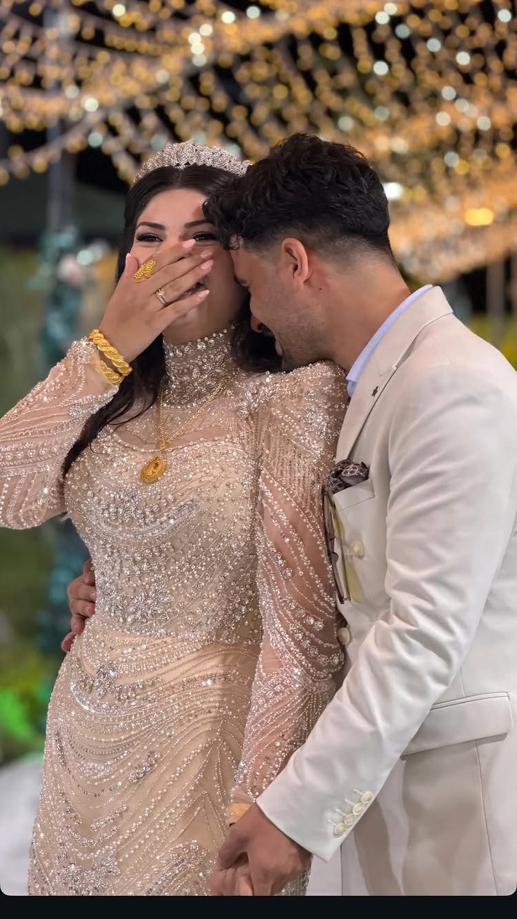 Couple in champagne and cream wedding attire posing under golden fairy lights.
